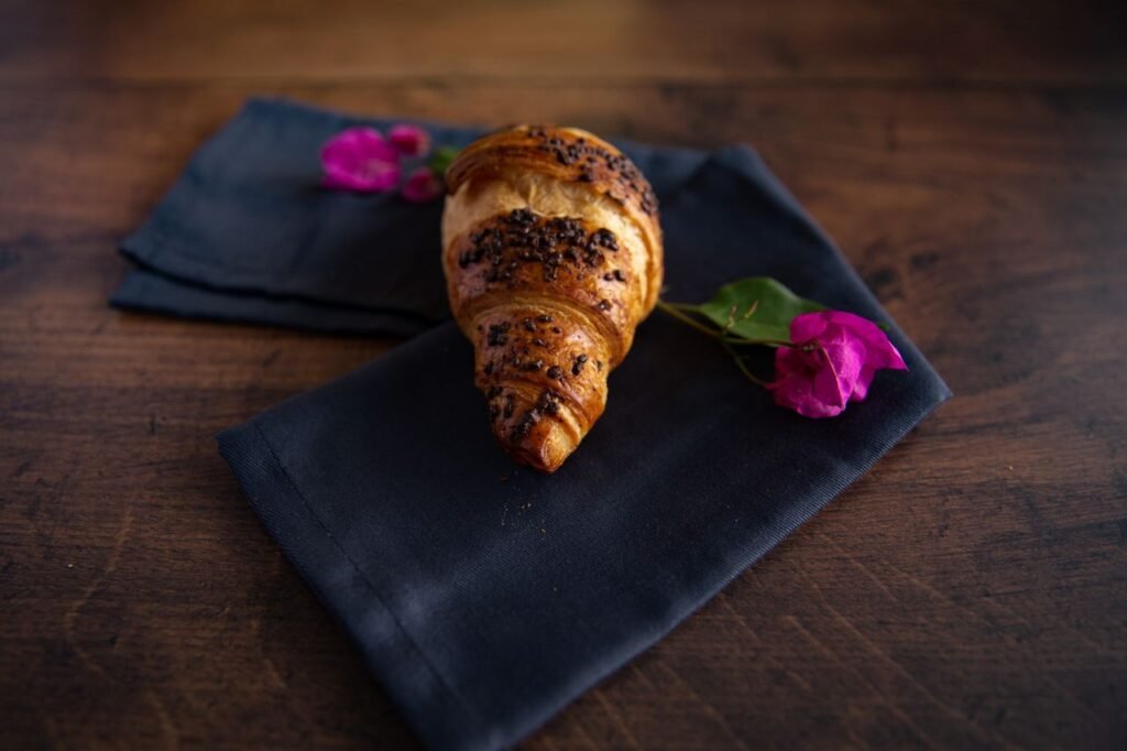 A freshly baked croissant on dark napkin with purple flowers, perfect for breakfast themes.